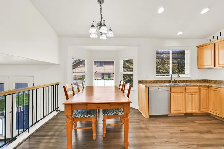 Open-concept dining and kitchen area featuring wood-finish flooring, recessed lighting, a bay window, natural wood cabinetry, and a double basin sink