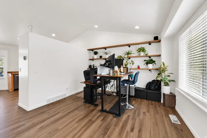 Vaulted ceiling with recessed lighting, wood-finish flooring, built-in shelving, and a large window