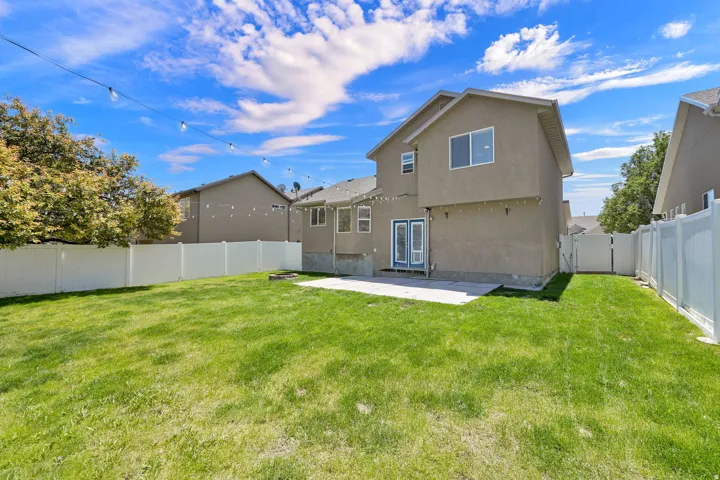 Expansive lawn area featuring a concrete patio, white vinyl fencing, double glass-panel doors, and an exterior stucco finish