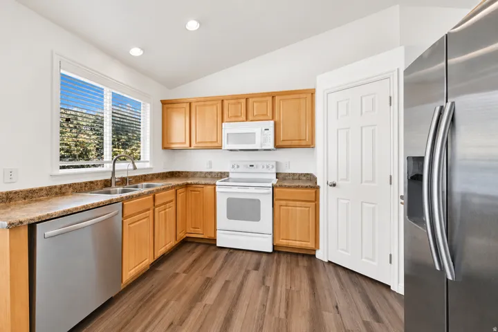 Kitchen featuring a stainless steel dishwasher, double basin sink with a gooseneck faucet, light wood cabinetry, and wood-finish flooring