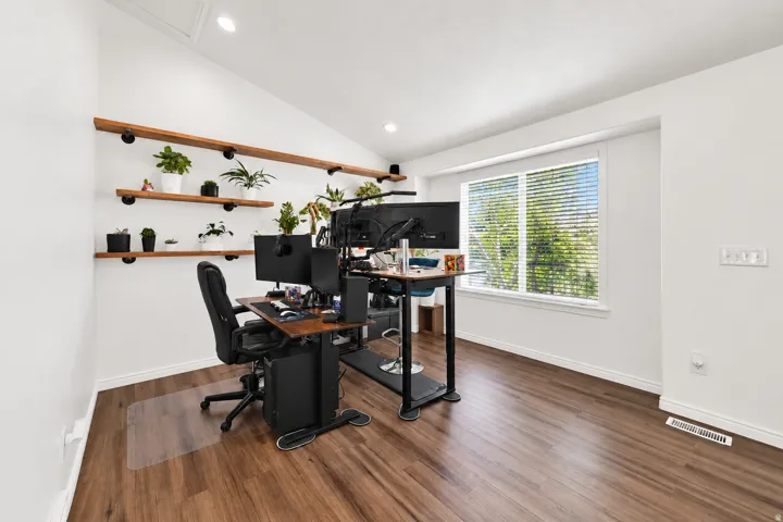 Vaulted ceiling with recessed lighting, wood-finish flooring, built-in floating shelves, and a large window with blinds