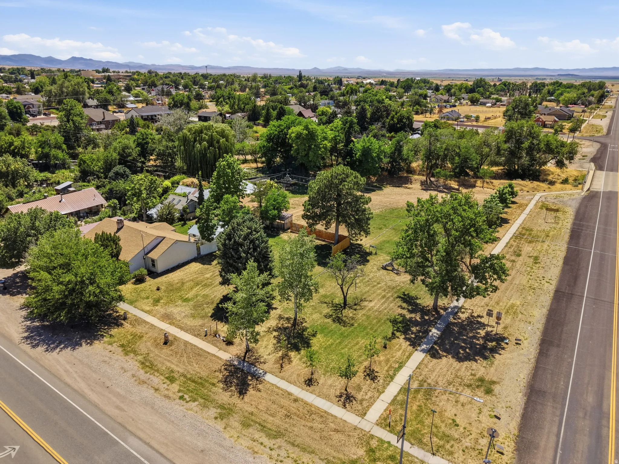 Expansive corner lot featuring a single-story residence with a tan exterior and brown shingle roof