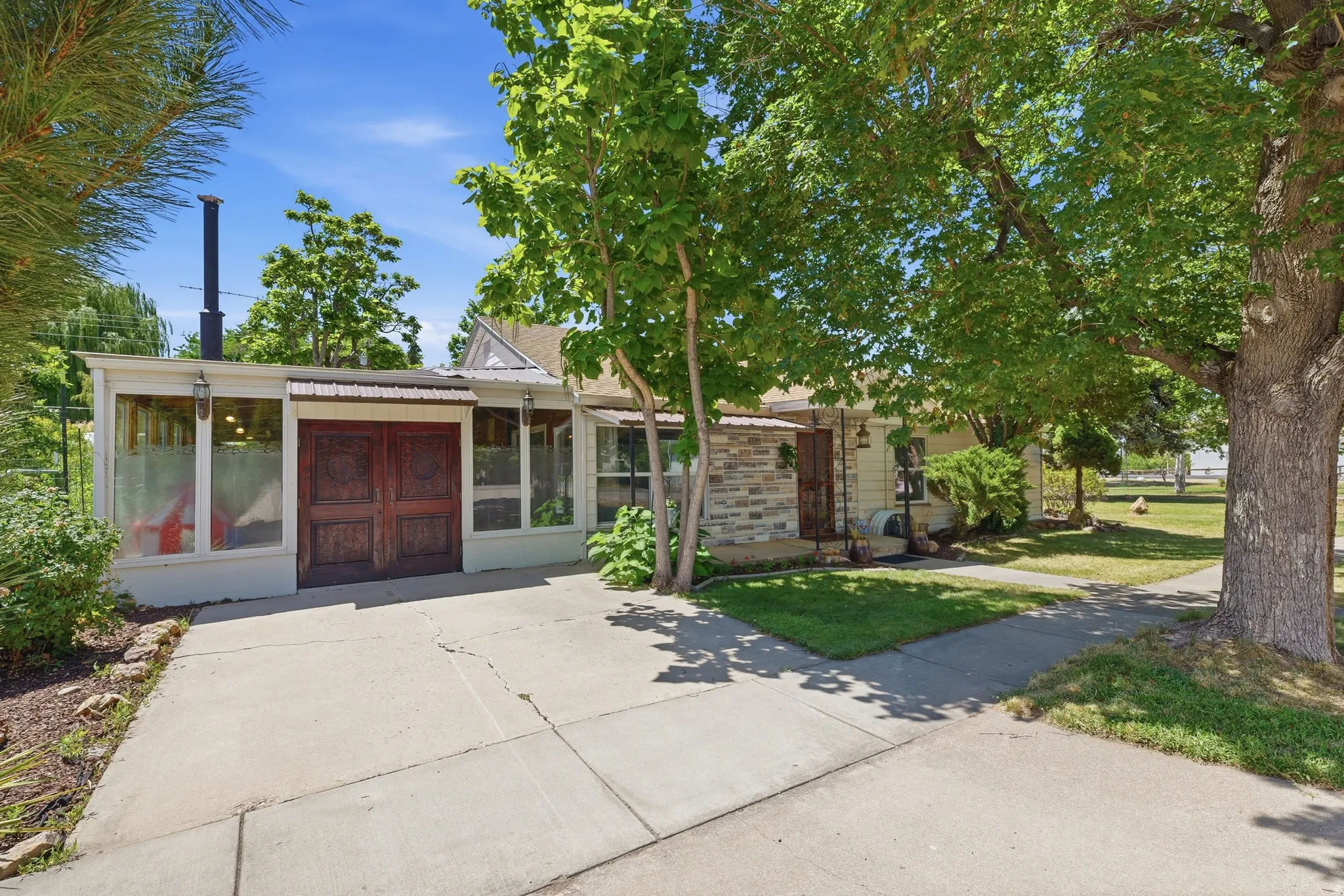 Property exterior featuring a stone facade, wood-paneled double entry doors, a covered porch, and mature trees providing natural shading