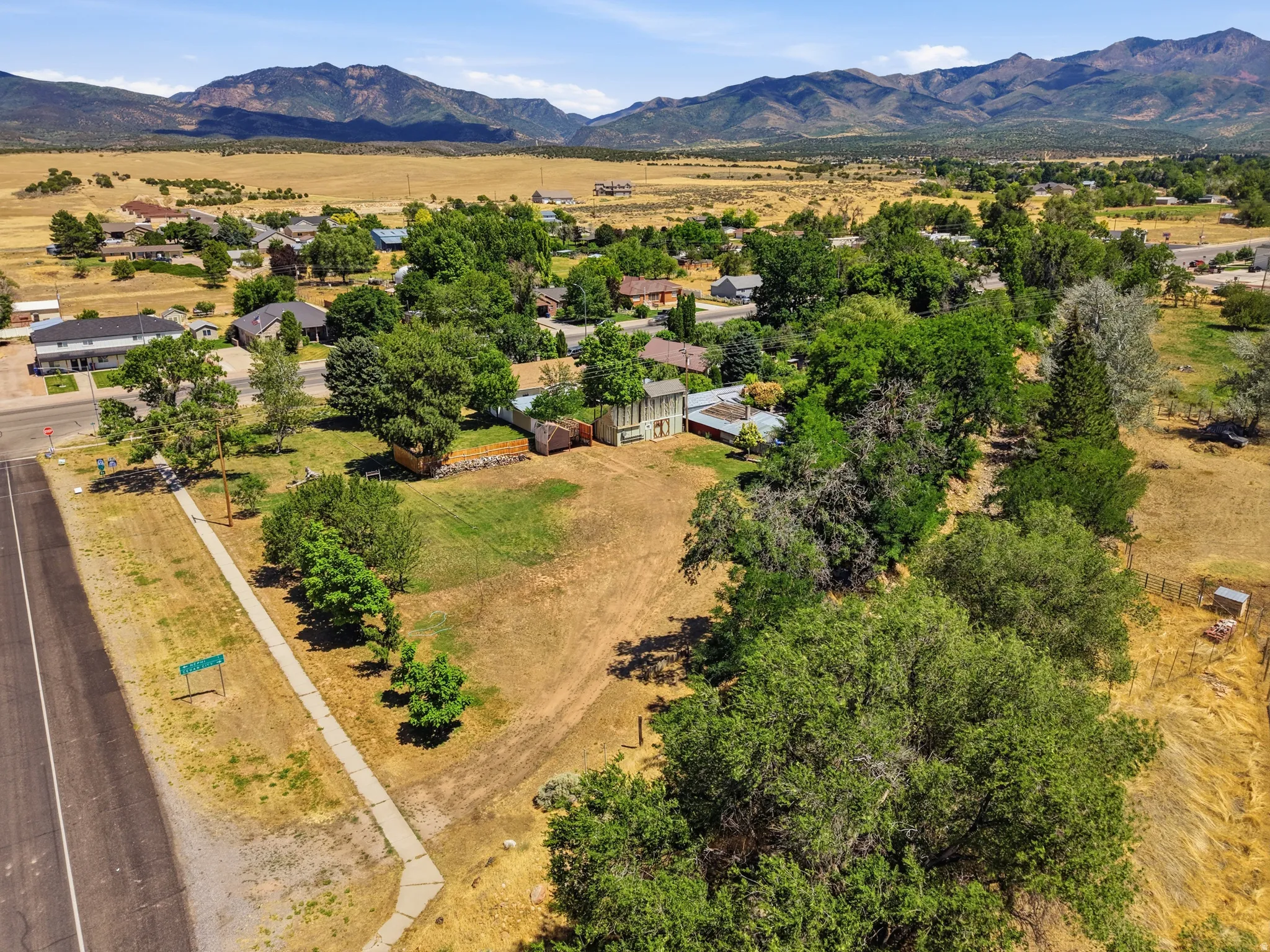 Expansive parcel featuring mature trees, open grassy areas, and a paved road with sidewalk access