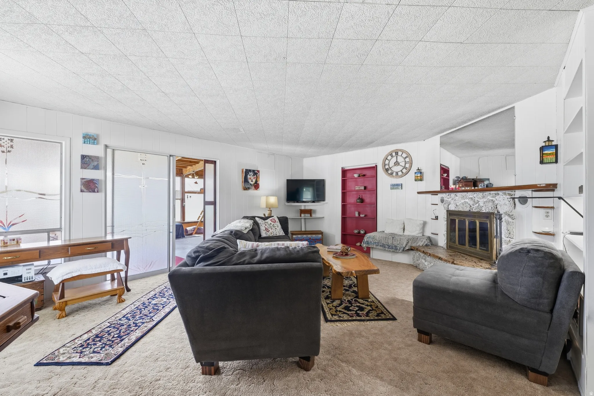 Living area featuring a stone fireplace with a wood mantle, built-in shelving, and carpeting