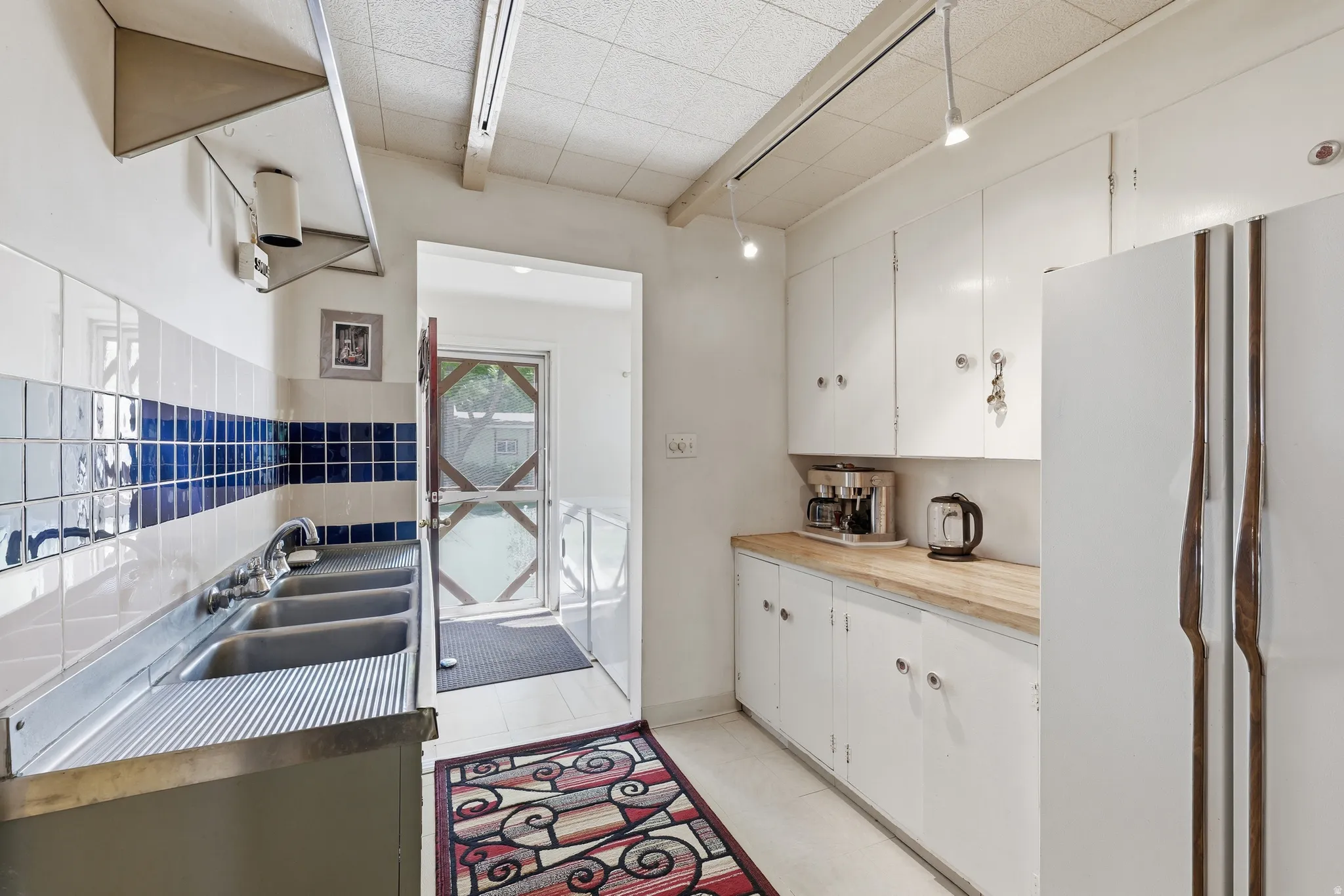 Kitchen featuring white cabinetry, light wood-finish countertops, a triple-basin stainless steel sink, and a tiled backsplash with blue accent rows