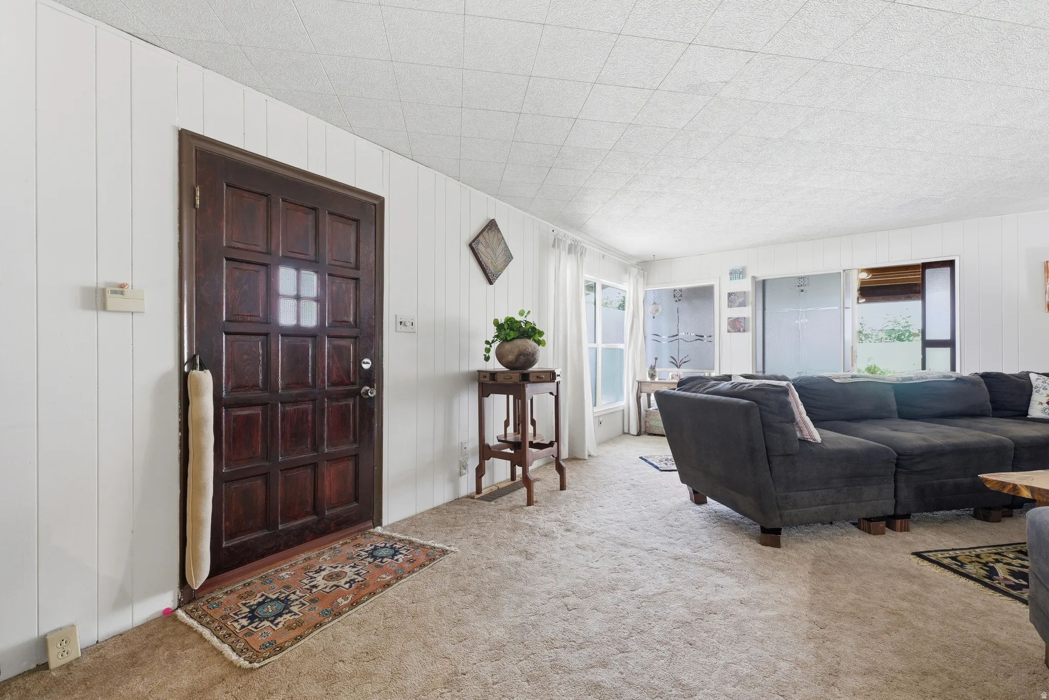 Paneled entry door with frosted glass insert, vertical paneled walls, and soft neutral carpeting