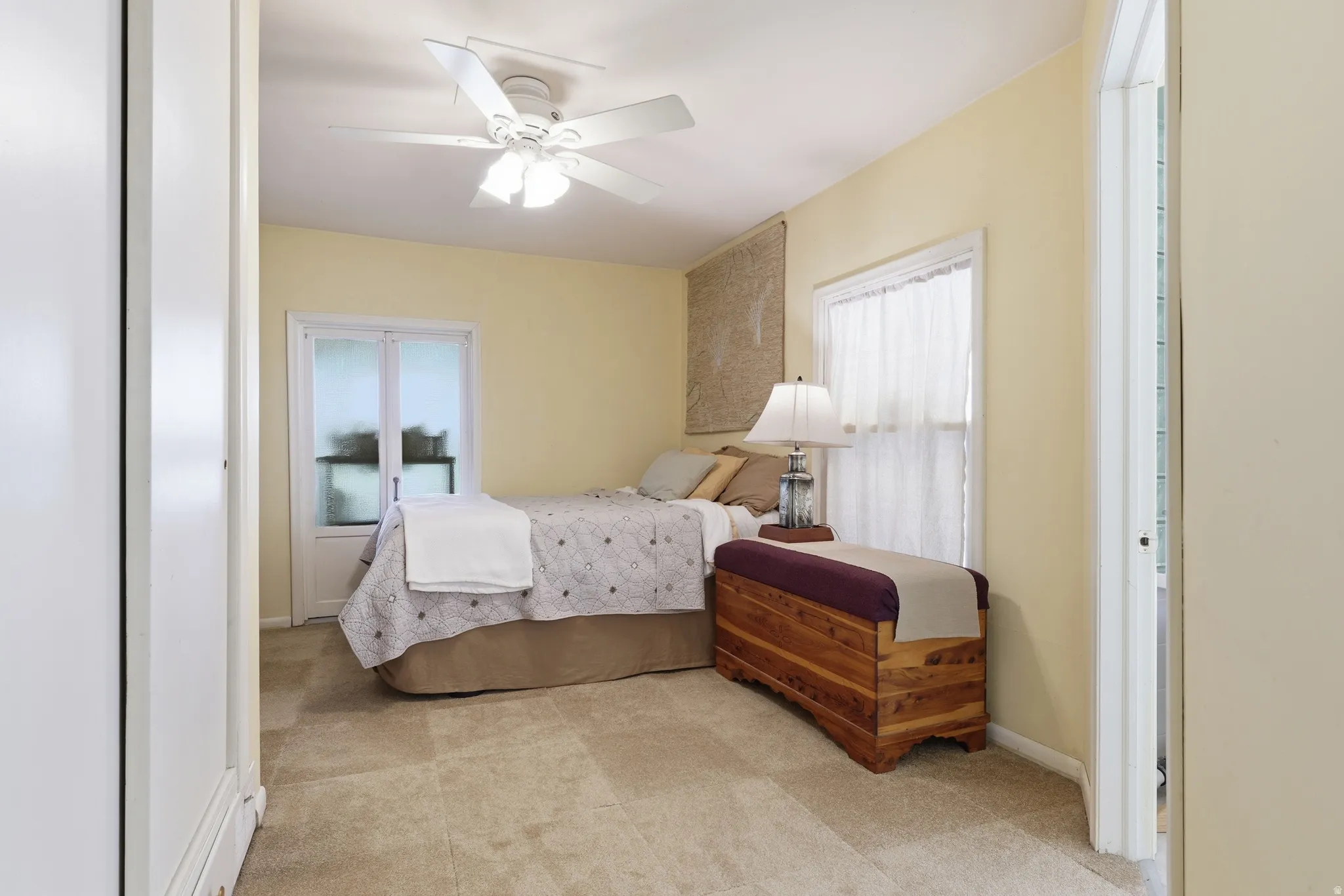 Carpeted room featuring a ceiling fan with integrated lighting, a window with sheer curtains, and a glass-paneled door
