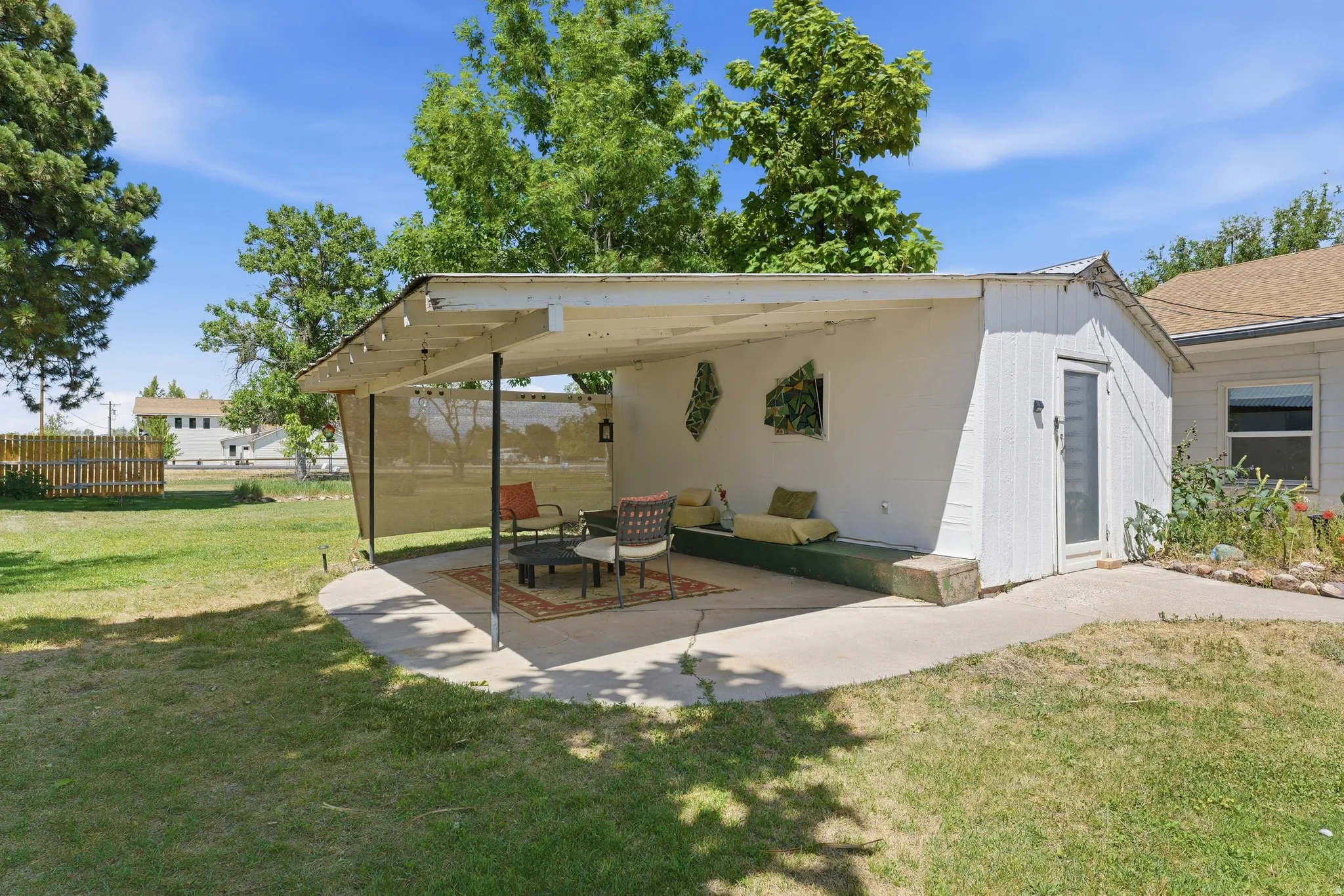 Expansive backyard featuring a concrete patio with an attached covered awning, a privacy screen, and an adjacent storage shed