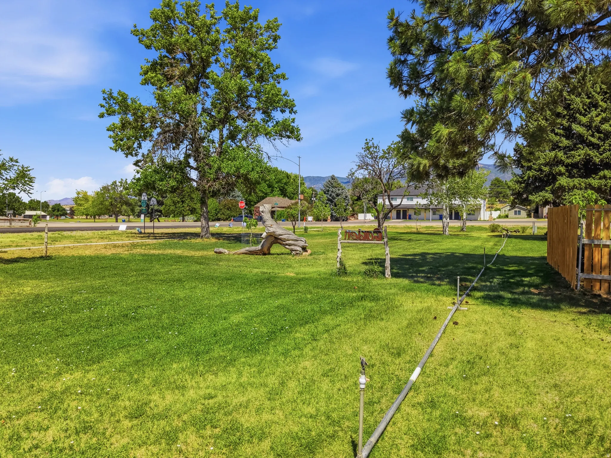 Expansive grassy area featuring mature trees and a partial wood fence