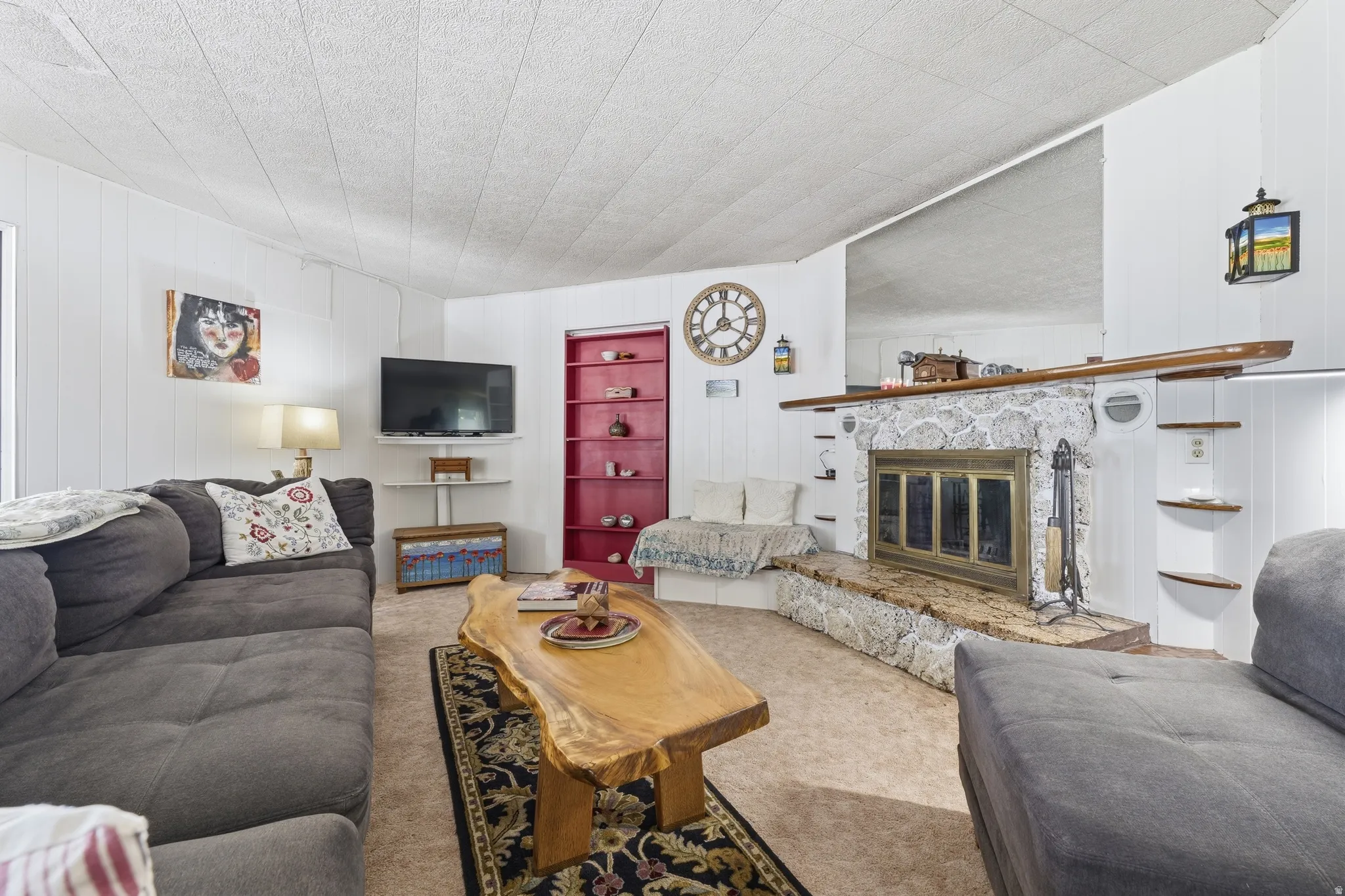 Living area featuring a stone-clad fireplace with a hearth, paneling, and a built-in red shelving unit
