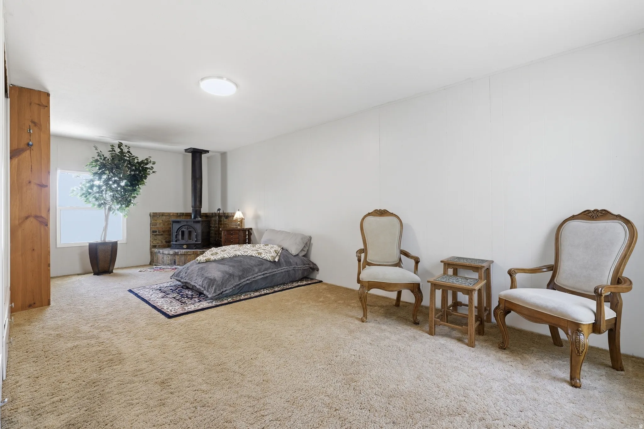 Spacious room featuring a central wood-burning stove with a brick hearth, wall-to-wall carpeting, white walls, and a recessed window