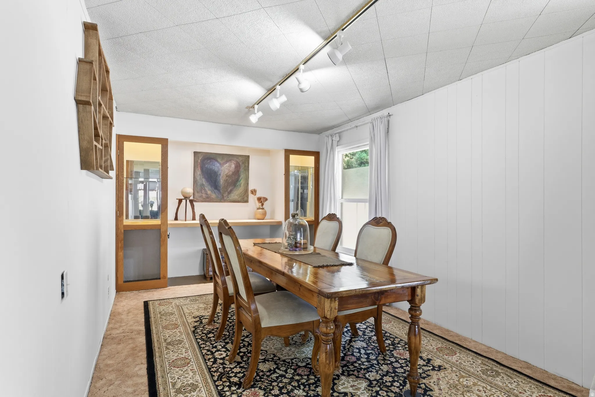 Dining area featuring a wood-finish table, recessed display niches with a wood shelf, and track lighting