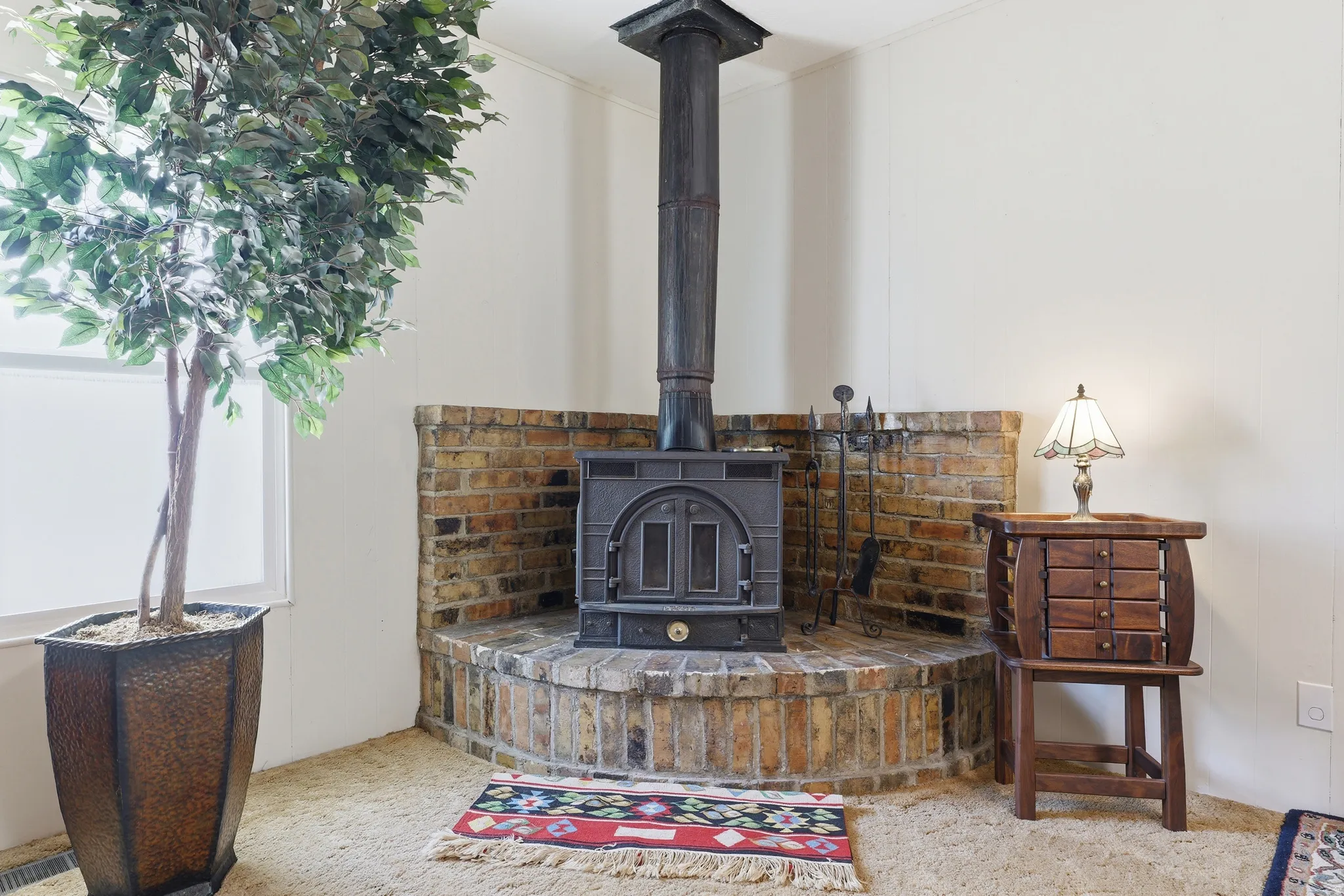Corner wood-burning stove with a brick surround and hearth, featuring a black metal flue