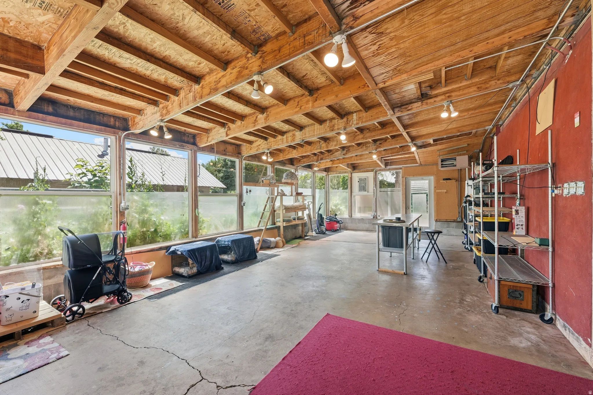 Enclosed sunroom featuring a pitched wood beam ceiling, exposed wood paneling, multiple windows, concrete flooring, and a red accent wall