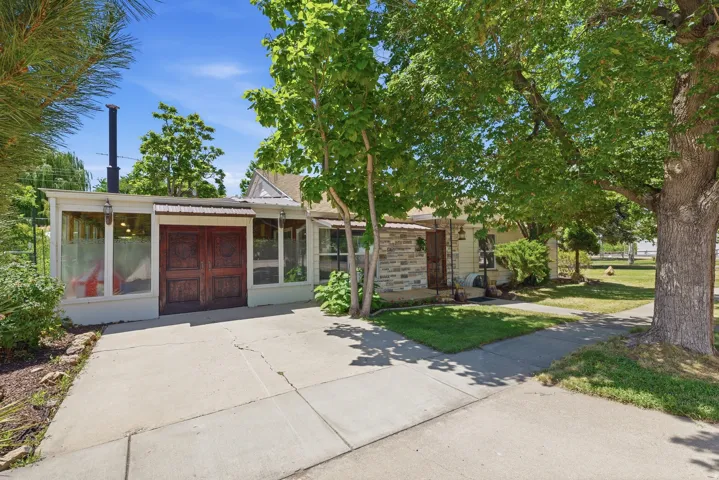 Property exterior featuring a stone facade, wood-paneled double entry doors, a covered porch, and mature trees providing natural shading