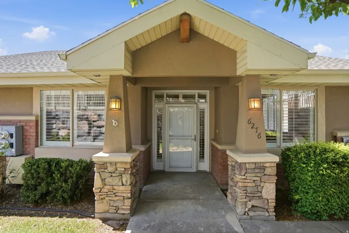 Covered entry featuring stacked stone columns, stucco exterior, and a gabled roofline
