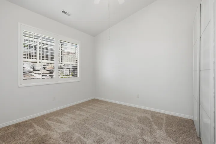 Room featuring a window with white louvered shutters, carpet flooring, baseboard trim, and a ceiling-mounted fan