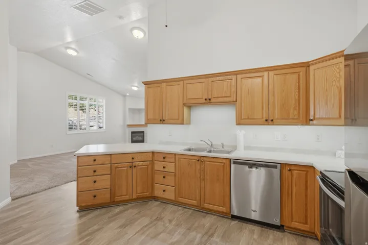 Open-concept kitchen featuring wood-finish cabinetry, light-toned countertops, stainless steel appliances, and wood-look flooring