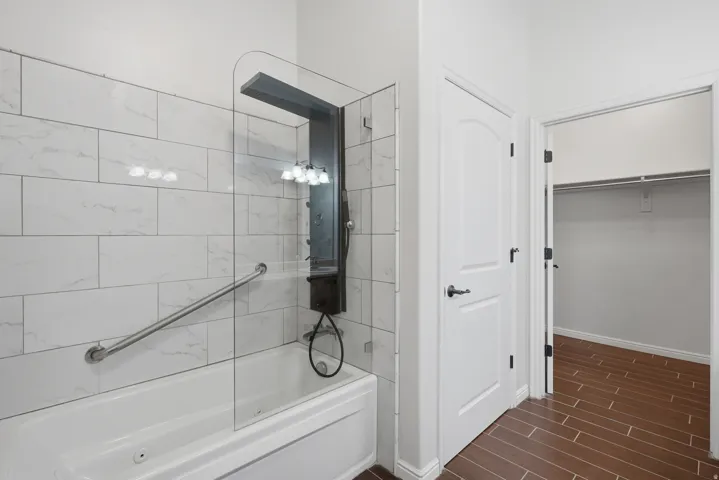 Jetted Bathtub with a glass shower panel, white subway tile surround, and a multi-function shower system