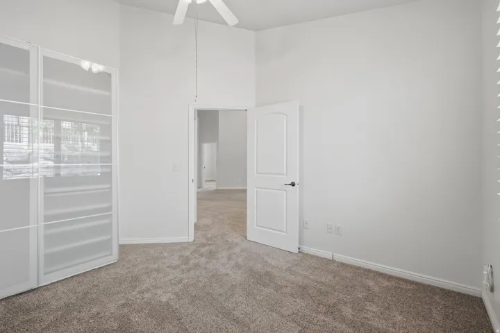 Carpeted room featuring a ceiling fan, a white paneled door, and a built-in closet with frosted glass doors