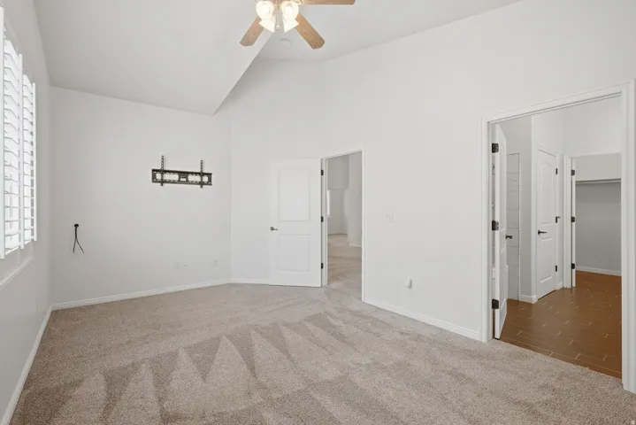 Spacious room featuring vaulted ceilings, neutral-toned carpet, a ceiling fan with integrated lighting, and white plantation shutters