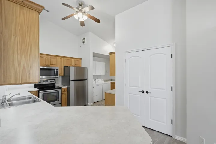 Kitchen featuring wood cabinetry, stainless steel appliances, a double basin sink, and a vaulted ceiling with a ceiling fan