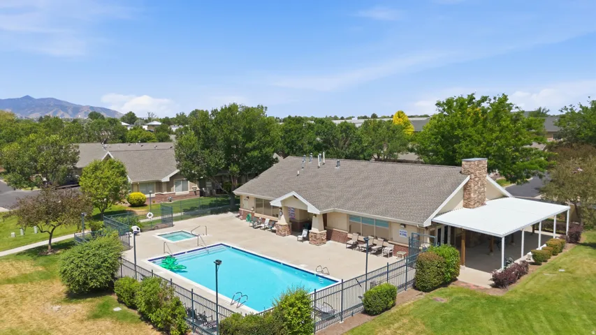 Community pool area featuring a rectangular swimming pool, a separate spa, and an adjacent building with a stone chimney and covered patio