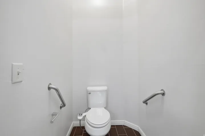 Bathroom featuring a white toilet with an attached bidet, brushed chrome grab bars, and wood-finish flooring