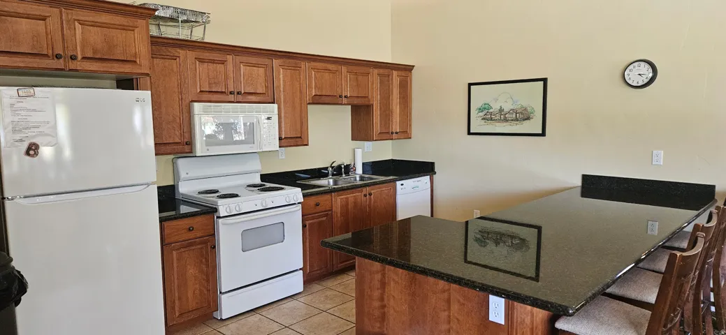 Kitchen featuring wood cabinetry, black countertops, stainless steel sink, and tile flooring