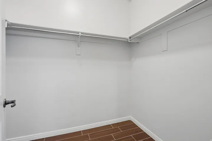 Walk-in closet featuring white walls, white trim, and wood-finish tile flooring