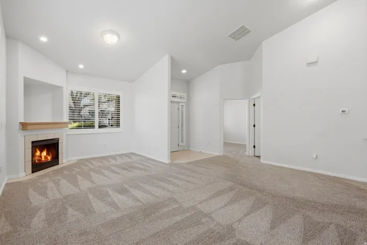 Living area featuring a fireplace with a light-toned wood mantel and tile surround, patterned carpet flooring, recessed lighting, and a window with plantation shutters