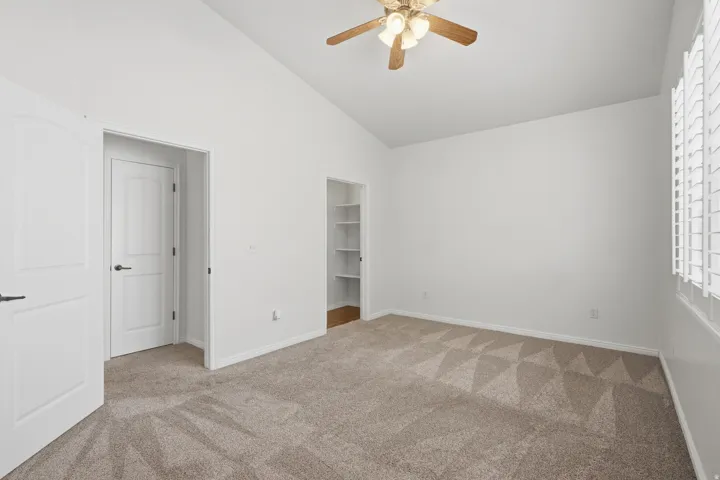 Carpeted room featuring a vaulted ceiling and a ceiling fan with integrated lighting