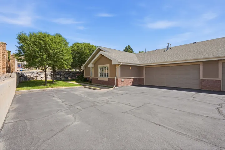 Exterior featuring stucco and brick siding, a multi-car garage, a shingle roof, and a paved parking area
