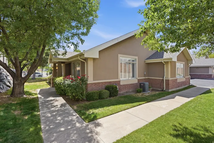 Stucco and brick exterior with a covered entry, mature landscaping, and a concrete pathway