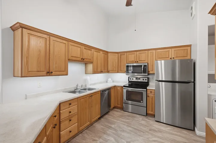 Kitchen featuring light wood cabinetry with crown molding, stainless steel appliances, a dual-basin sink, and light-toned countertops