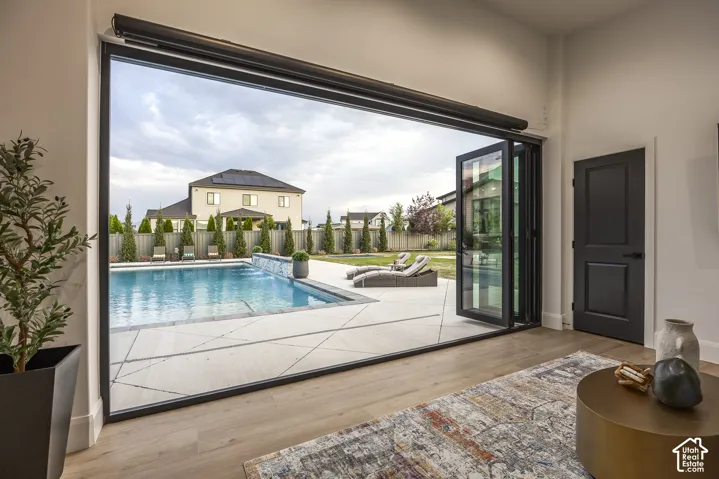 Expansive bi-fold glass doors open to a backyard featuring a swimming pool with a waterfall element, a surrounding patio, and mature landscaping
