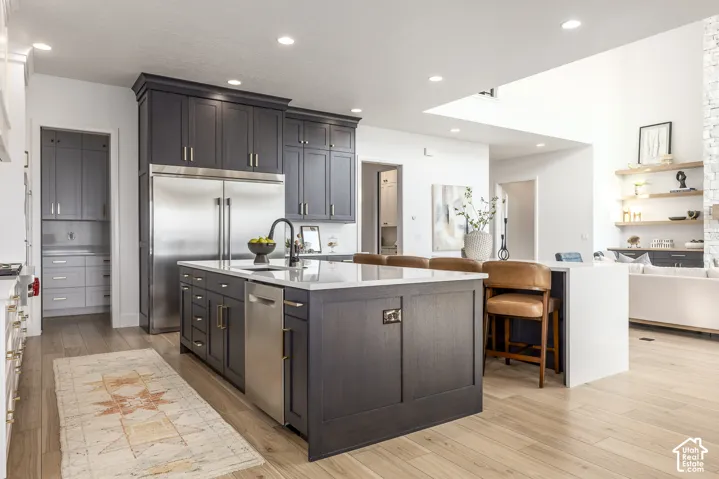 Spacious kitchen featuring an expansive center island with seating, stainless steel appliances, dark wood-finish cabinetry, recessed lighting, and wood-finish flooring