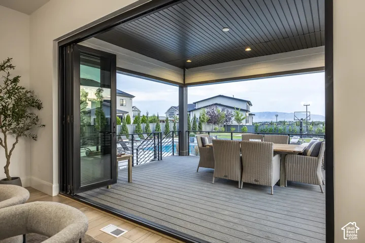 Expansive covered patio featuring a wide-plank deck, recessed lighting, and a black metal railing overlooking a swimming pool