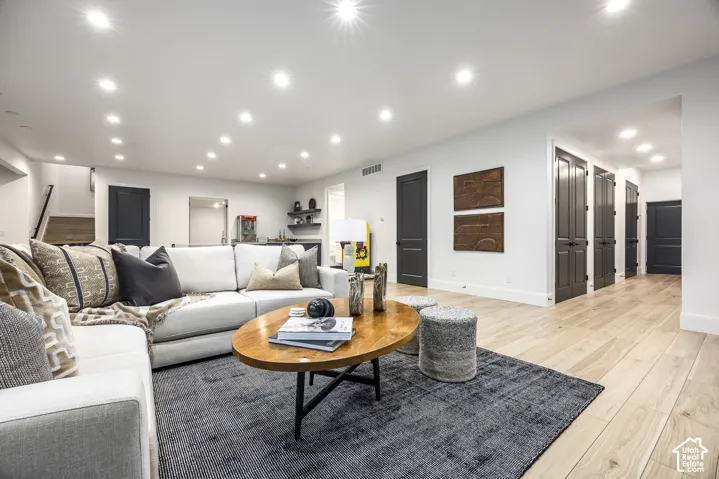 Spacious living area featuring light wood-finish flooring, recessed lighting, and white walls