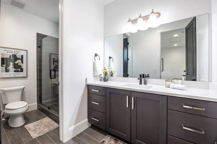 Contemporary bathroom featuring a spacious vanity with white countertop, dark wood-finish cabinetry, and an undermount sink with a black faucet