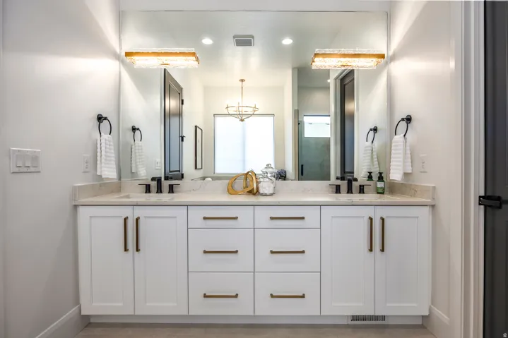 Double vanity featuring white cabinetry with gold-finish hardware, a light-toned countertop, and dual black-finish faucets