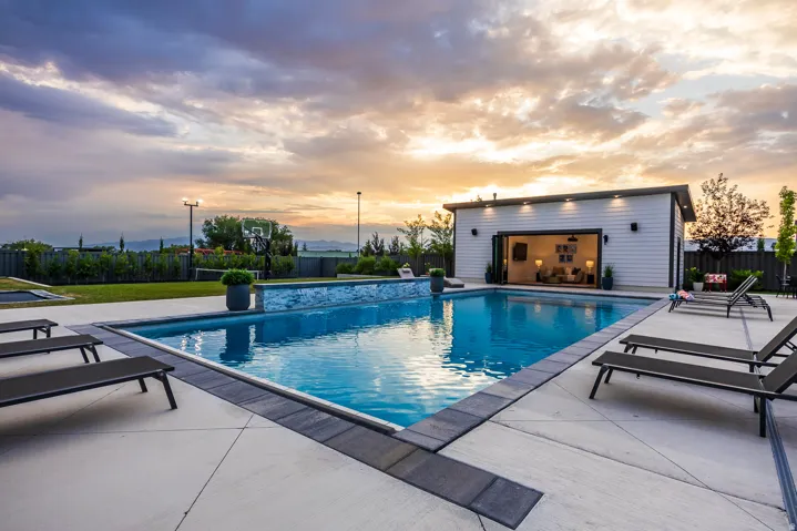Custom pool house with bi-fold doors, a rectangular swimming pool, and concrete decking