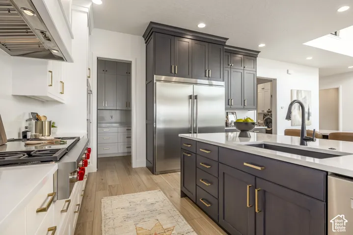Gourmet kitchen featuring a substantial central island with an undermount sink, a stainless steel refrigerator, and wood-finish flooring