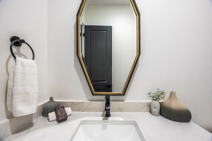 Geometric framed mirror with a gold accent, set above a white countertop featuring subtle veining