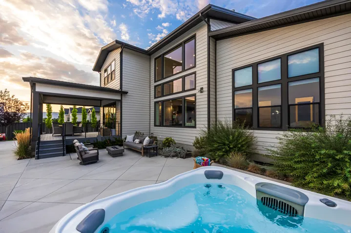 Outdoor patio featuring a hot tub, expansive concrete surfacing, a covered deck with dark railings, and a two-story exterior with large black-framed windows