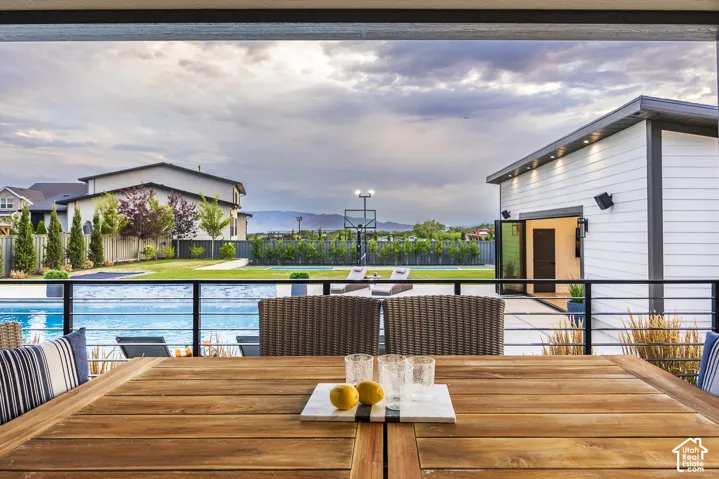 Expansive outdoor living area featuring a wooden patio table, glass panel railing, and a swimming pool