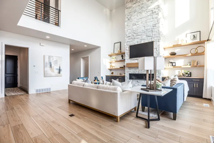 Two-story living area featuring a stacked stone fireplace with a built-in linear electric fireplace, soaring ceilings, and wood-finish flooring