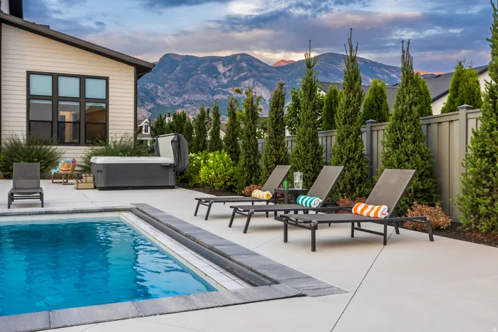 Outdoor patio featuring a rectangular swimming pool with a stone coping, an adjacent hot tub, and concrete decking