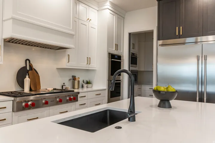 Kitchen island featuring a black undermount sink with a gooseneck faucet, white countertop, and stainless steel French door refrigerator